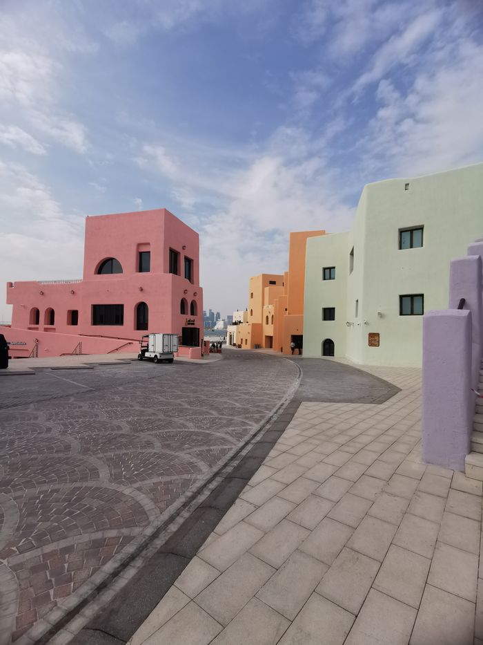 Vibrant pastel-colored buildings line a narrow street in the Old Doha Port, Qatar.